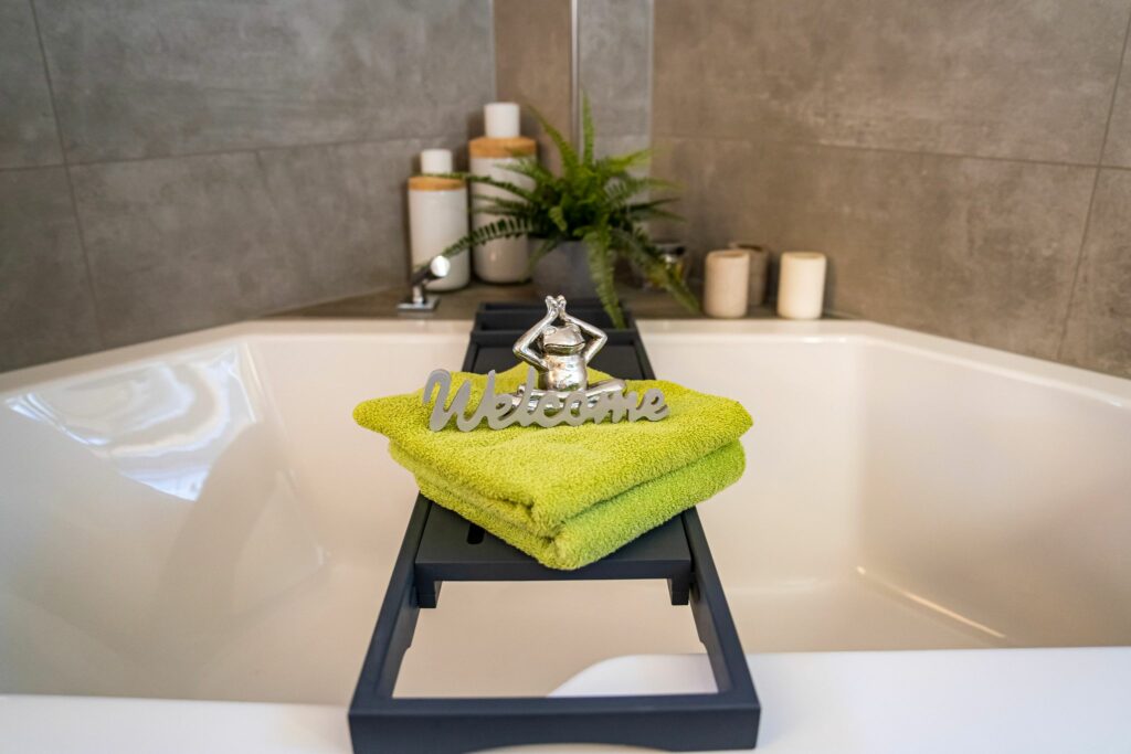 Moderne Badewanne mit grüner Handtuchdekoration, Kerzen und Pflanze im Hintergrund – stilvolles Badezimmer von KLU-BAD